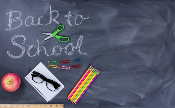 Back to school text on erased chalkboard with student supplies