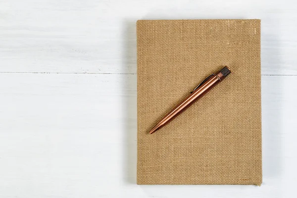 Vintage metal pen and burlap covered notepad on white desktop