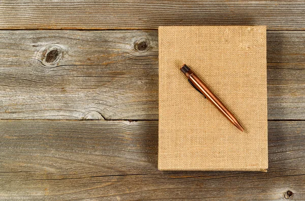 Vintage metal pen and burlap covered notepad on old wooden deskt