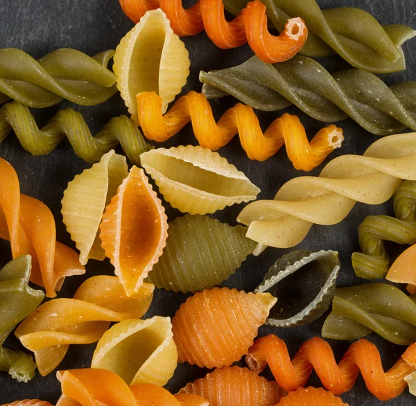 Colorful raw pasta on natural black slate background
