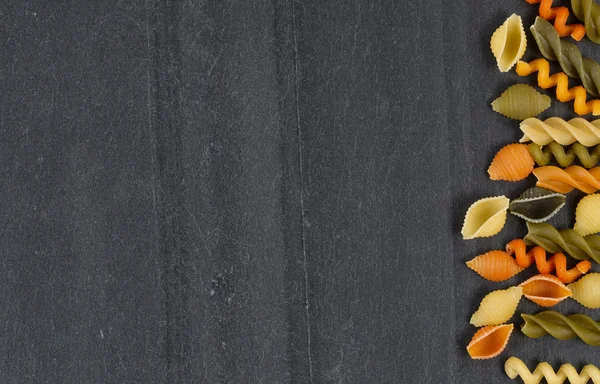Colorful raw pasta on natural black slate in horizontal layout