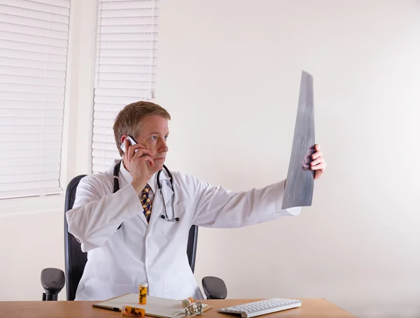 Doctor looking over x-ray chart while communicating on cell phon