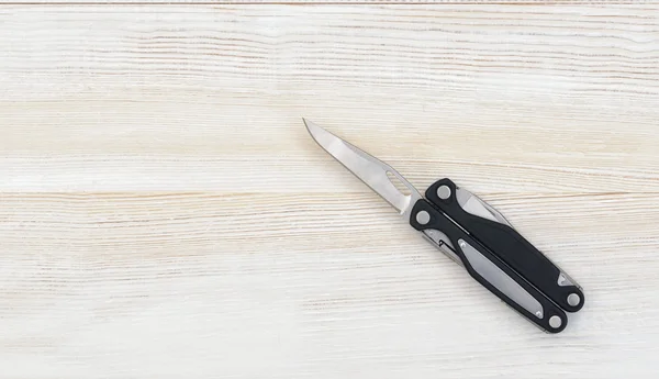 Multi tool with black handles on a white wooden background. Top view of desktop