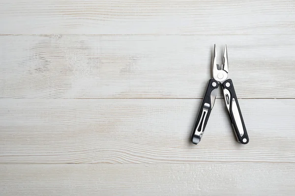 Multi tool with black handles on a white wooden background. Top view of desktop