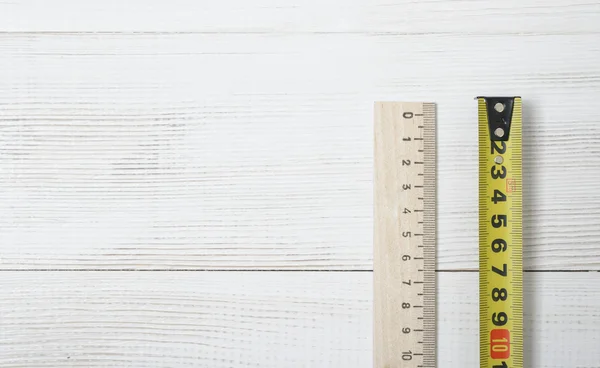 Top view of  tape measure and ruler on white wooden DIY workbench.