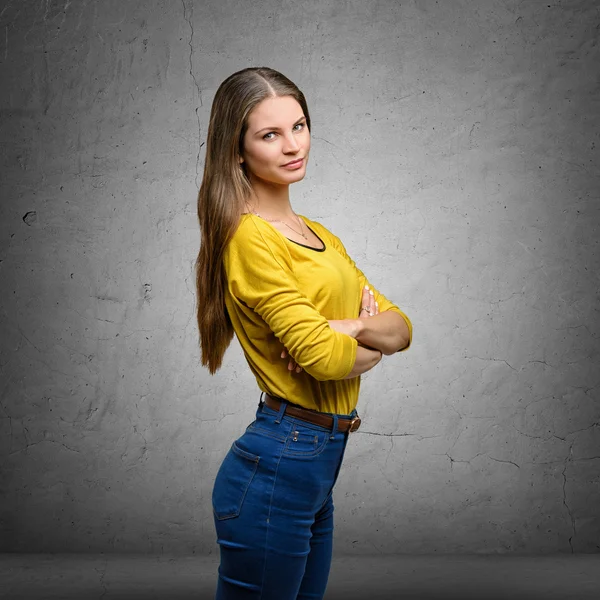 Woman wearing yellow blouse and jeans, standing sideways with crossed arms looking directly in camera