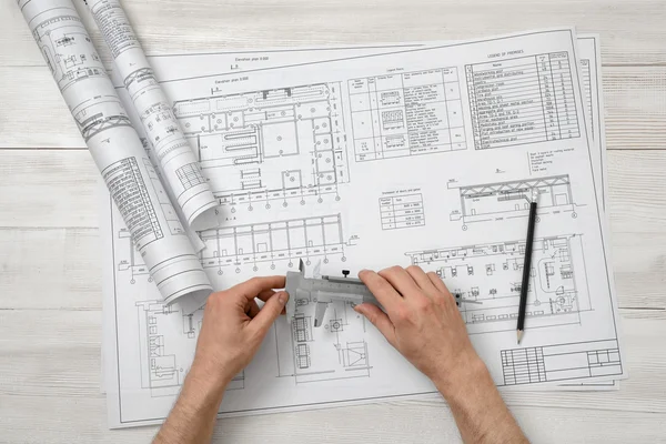 Hands of architect holding a centimeter device over drawing layout in top view.