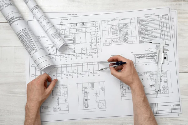 Close-up hands of man holding an engineering divider over drawing plan in top view.