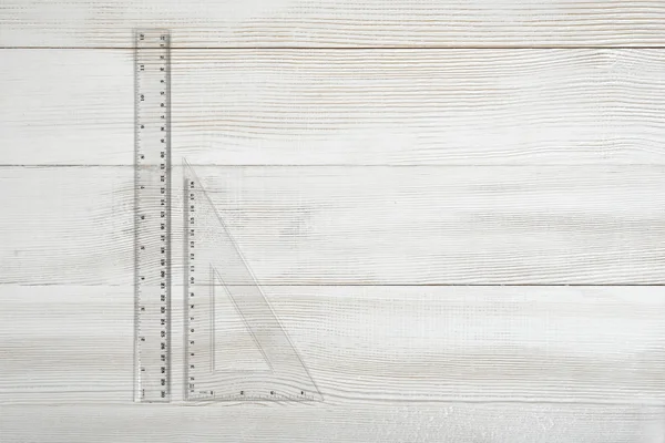 Plastic triangular and straight-edge ruler on wooden table.