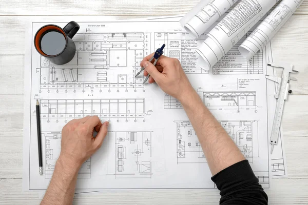 Close-up hands of man holding an engineering divider over drawing plan in top view