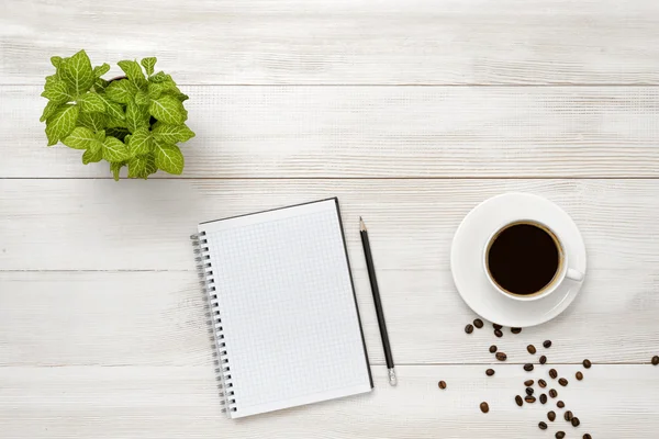 Workplace with cup of coffee, indoor plant, empty notebook and pencil on wooden surface
