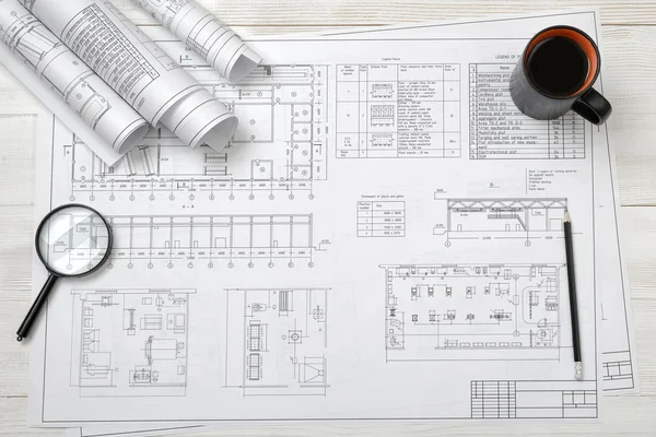 Top view of draftsmans workplace with plan, magnifier, pencil, mug coffee and rolled drafts