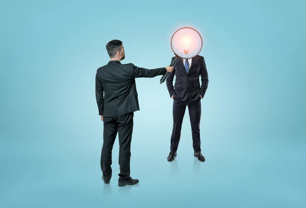 Businessman directing magnifying glass on lamp-headed man