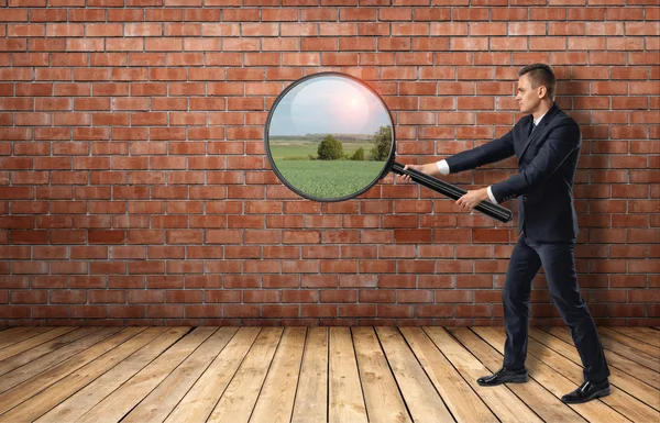 Businessman looking at red brick wall through a magnifier and seeing nature landscape