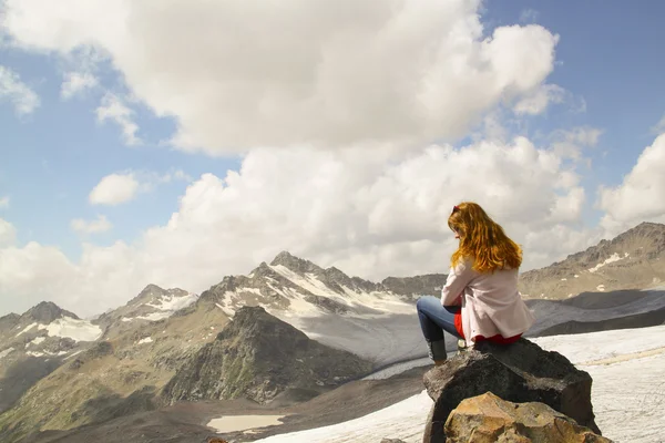 Young girl sitting on the edge of a cliff and looking at the sky