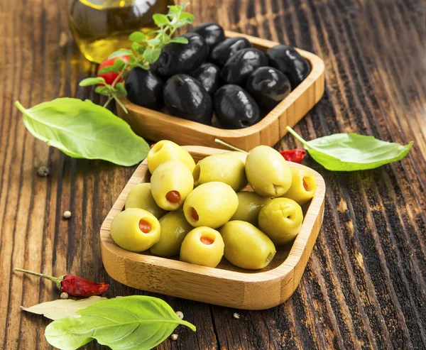 Organic green and black olives in wooden bowls with spices
