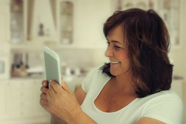 Attractive mature woman reading a book on tablet computer.