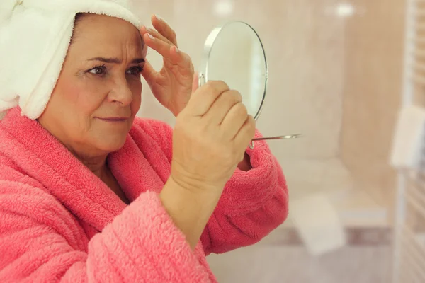 Portrait of an attractive middle aged woman looking into a mirror in the bathroom