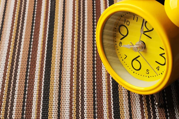 Close up yellow retro alarm clock on color mat shows 8 oclock