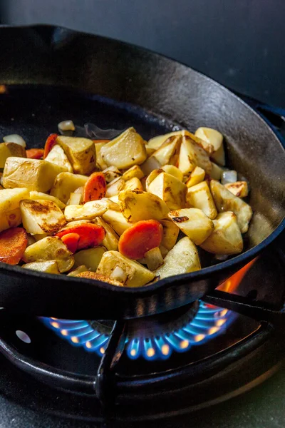 Potatoes in skillet over a fire.