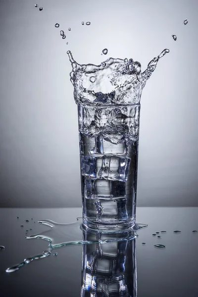 Ice splashes into water glass.