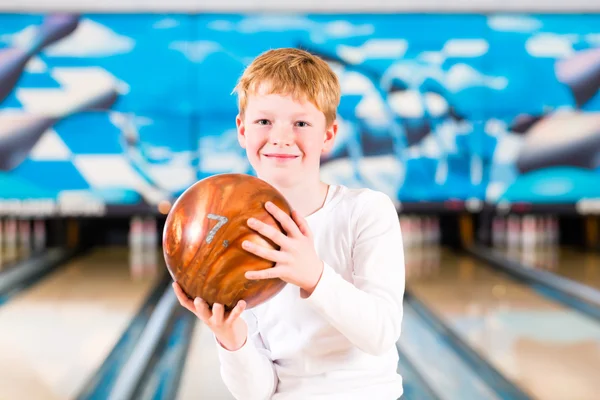 Child bowling with ball in alley