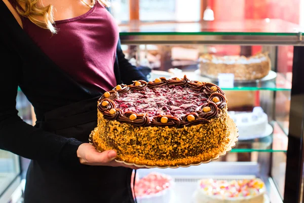 Female baker presenting cake in confectionery