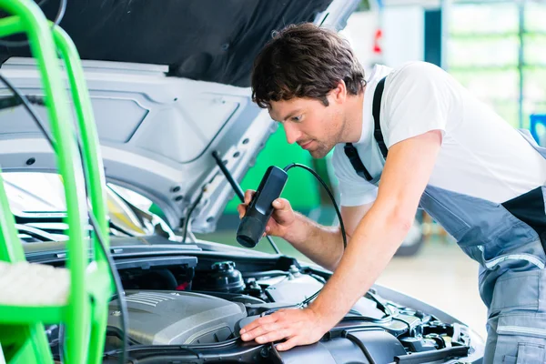 Mechanic with diagnostic tool in car workshop