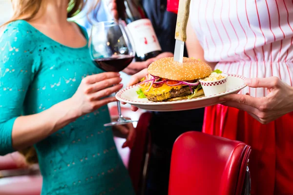 People in American diner with burger and wine