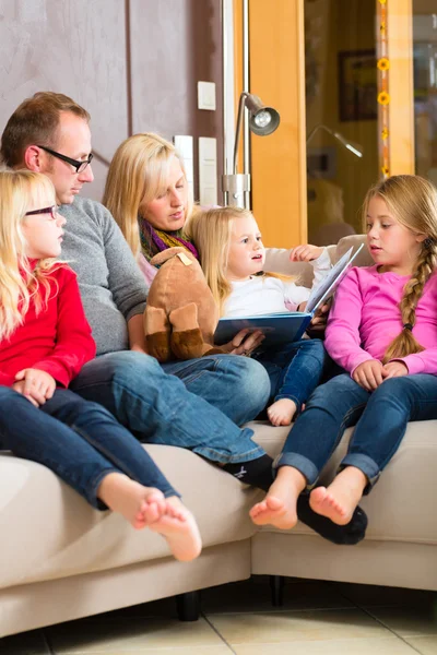 Family reading story in book on sofa in home