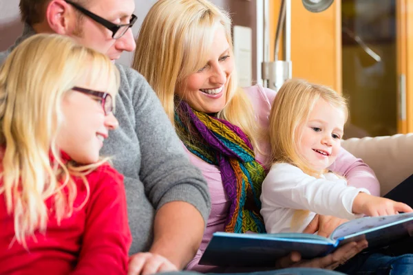 Family reading story in book on sofa in home