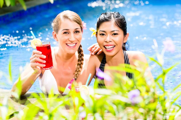 Women in Asian hotel pool drinking cocktails