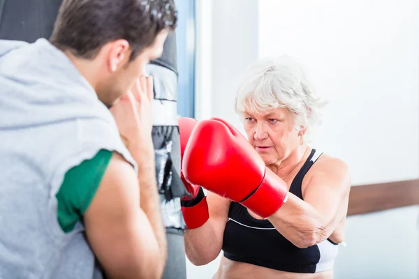 Senior woman with trainer in boxing sparring