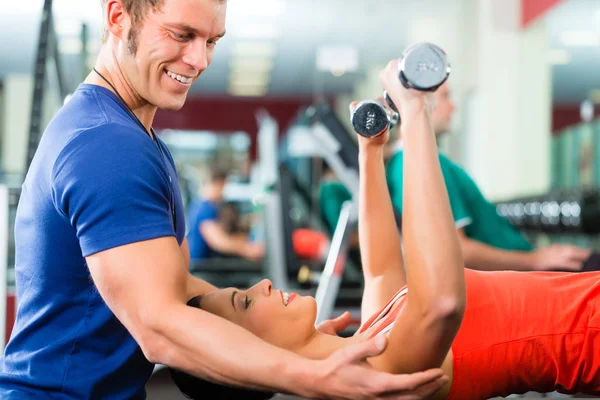 Woman and Personal Trainer in gym with dumbbells