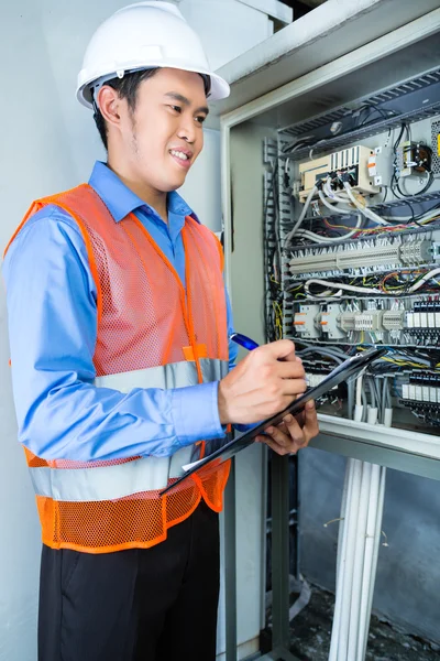 Asian Electrician at panel on construction site