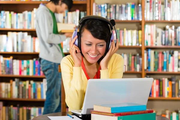 Woman in library with laptop and headphones learning