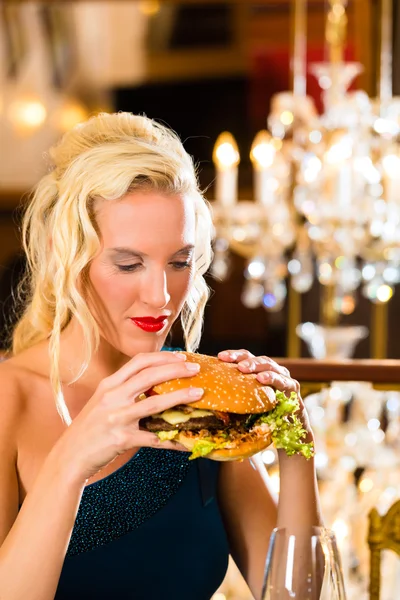 Woman in fine restaurant, she eats a burger