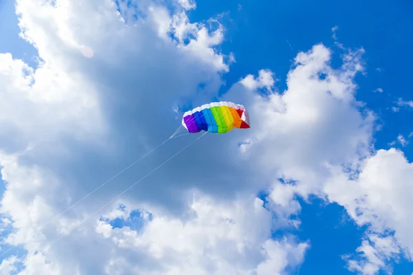 Rainbow colored childs kite on blue sky with clouds