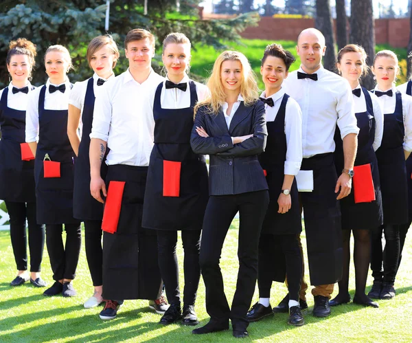 Large group of waiters and waitresses standing in row.