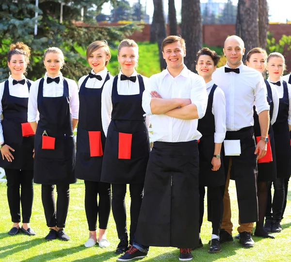 Large group of waiters and waitresses standing in row.