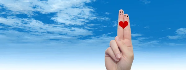 Concept or conceptual human or female hands with two fingers painted with a red heart and smiley faces over cloud blue sky background banner