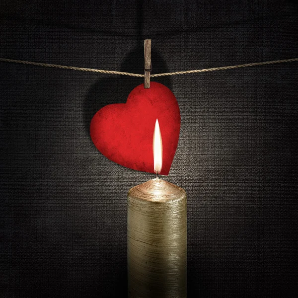 Burning candle and red paper heart on a rope