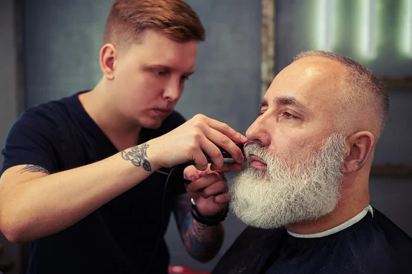 Close up of barber trimming clients beard in barber shop