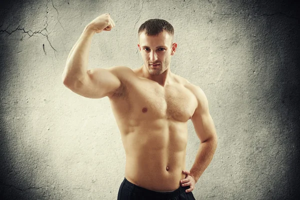 Man showing biceps on right arm over concrete wall