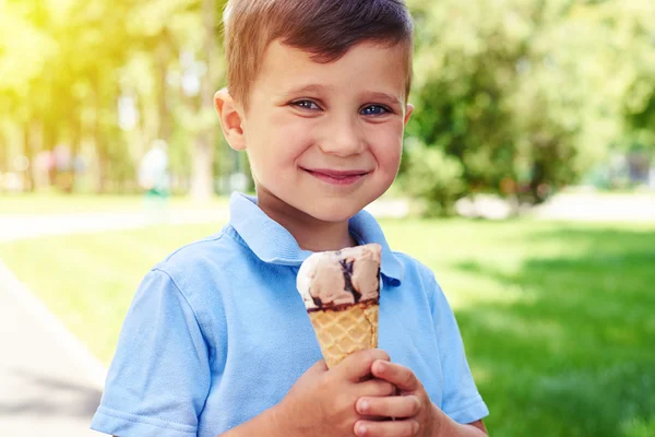 Small boy with beautiful eyes holding ice-cream in the park.