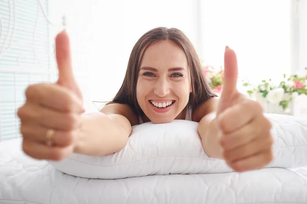 Portrait of woman with broad smile on bed with hands on cushion