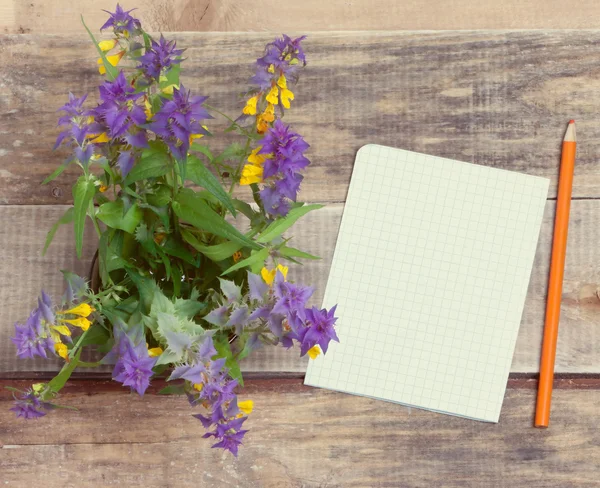 Bouquet of wild flowers and a piece of paper with a pencil on a wooden table.