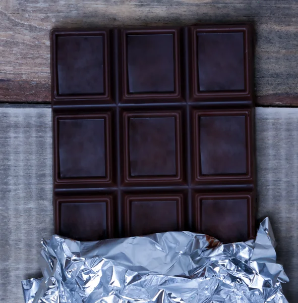 Open the foil-wrapped chocolate bar lying on a wooden surface