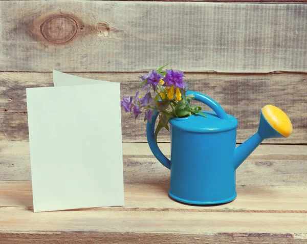 Little watering can, flowers and a blank sheet of paper