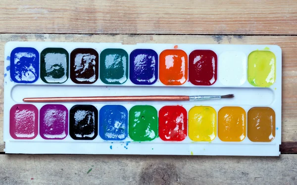 Palette of watercolor paints, glass of water and a piece of blank paper